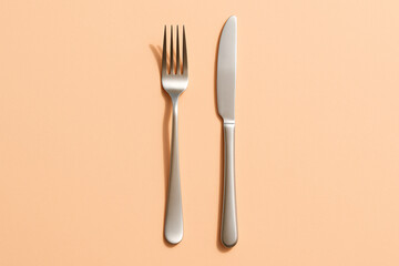 Stainless steel fork and knife neatly arranged side by side on a peach-colored background