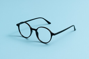 Stylish round black eyeglasses placed on a pastel blue background with a clean, minimal aesthetic