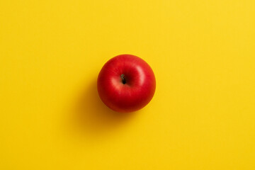 Bright red apple centered on a vibrant yellow background creating a bold and colorful contrast.