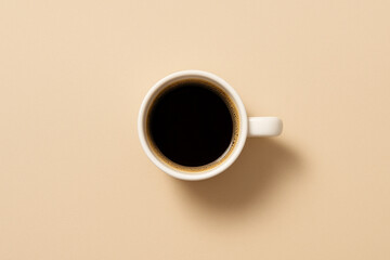 Top view of a white cup filled with black coffee placed on a neutral beige background