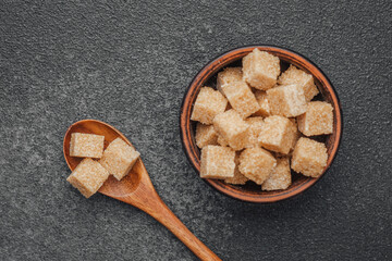 Brown sugar cubes in a wooden bowl with a spoon on a dark surface