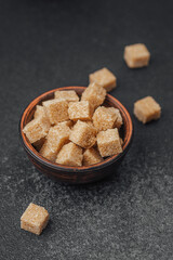 Brown sugar cubes in a wooden bowl on a dark countertop