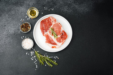 Uncooked beef steaks on white plate with rosemary and spices