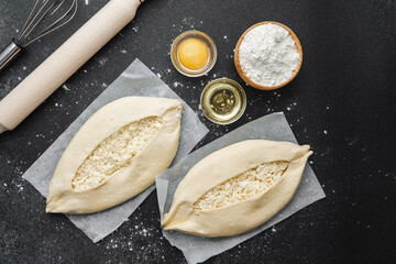 Top view of ingredients and two uncooked khachapuri on floured black table