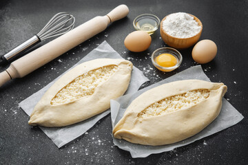 Top view of ingredients and two uncooked khachapuri on floured black table