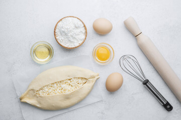 Unbaked khachapuri with cheese on parchment and baking ingredients