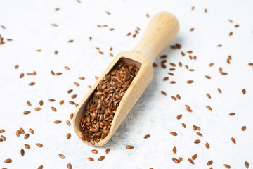 Flax seeds in a wooden scoop on a light background with scattered seeds