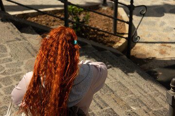 Top view of red haired tourist woman walking down stairs in an old town on a sunny day