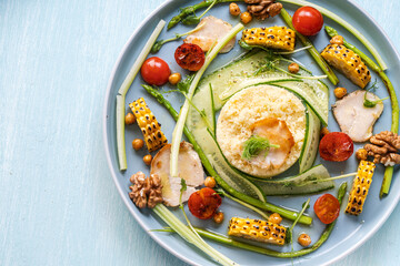 Couscous with chicken pieces, cucumbers, asparagus and corn, tomatoes and walnuts on a blue plate on a light background. View from above. Space for text.