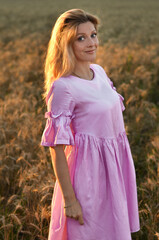 Woman with long hair in pink dress stands in golden wheat field during sunset, highlighting natural...