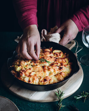 Chef preparing cheesy potato dish with rosemary garnish