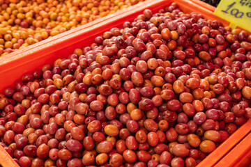 Close-up of red and orange olives displayed in plastic tray at Turkish outdoor market with handwritten price label