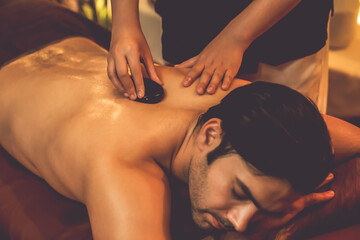 Hot stone massage at spa salon in luxury resort with warm candle light, blissful man customer...