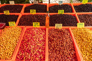 Assorted olives displayed in plastic bins at Turkish outdoor market with handwritten price signs