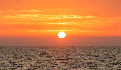 Naklejka premium The sun is setting over the ocean, casting a warm glow on the water