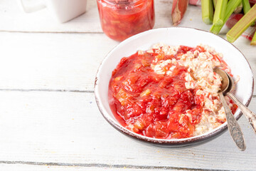 Sweet rhubarb oats in breakfast bowl Summer tasty healthy vegan food. Dietary breakfast or snack. Organic rhubarb overnight oatmeal, with rhubarb jam, yogurt, on white wooden table copy space