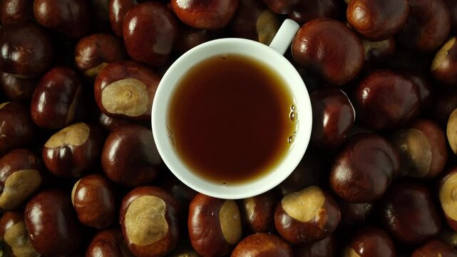 Chestnut chai or Conkers tea in white cup, top view. Healthy drink on chestnuts fruit background. 4K video, Rotation.