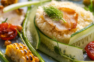 Couscous with chicken pieces, cucumbers, asparagus and corn, tomatoes and walnuts on a blue plate on a light background. Close-up.