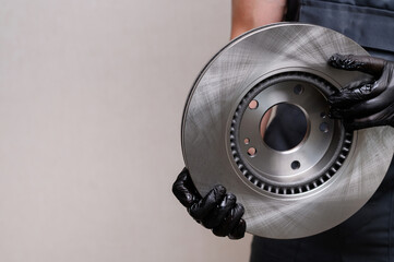 Auto mechanic holds new brake disc in hands in black gloves, close-up, copy space. Concept of auto...