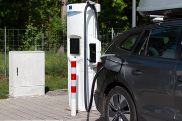 Fototapeta premium Electric car on charging station. Battery EV vehicle plugged and getting electricity from renewable power generations solar panel, wind turbine. Vehicle being charged.