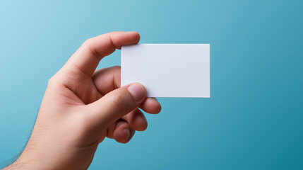 Obraz premium Hand holding a blank white business card against a blue background. 