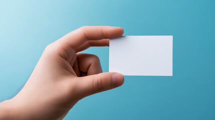Obraz premium Hand holding a blank white business card against a blue background. 