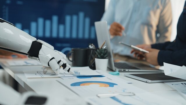 A futuristic collaboration scene showing a robot arm interacting with business professionals in a modern office setting, highlighting technology integration and teamwork.Noogenesis