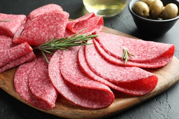 Slices of delicious sausage with rosemary served on black table, closeup