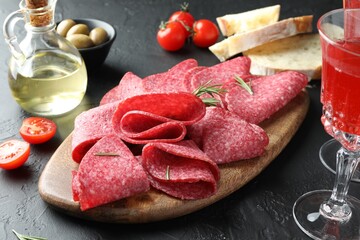Slices of delicious sausage with rosemary served on black table, closeup