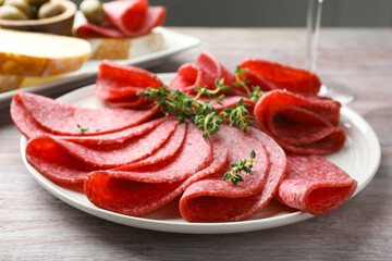 Slices of delicious sausage with thyme served on light wooden table, closeup