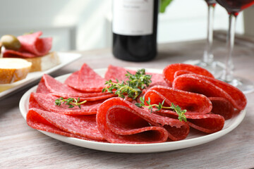 Slices of delicious sausage with thyme served on light wooden table, closeup