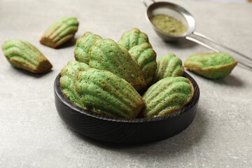 Tasty madeleine cakes and matcha powder on light table, closeup