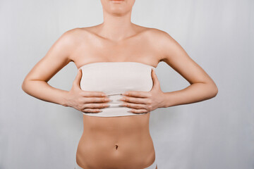 Patient recovering after breast reduction surgery, holding her breasts covered with elastic...