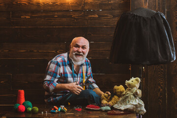 Happy senior man knit. Old man knitting at home. Elderly men making clothes for toys with needles...