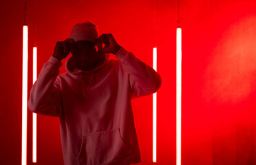 African American man adjusting beanie in red-lit studio, with neon tubes and haze, copy space