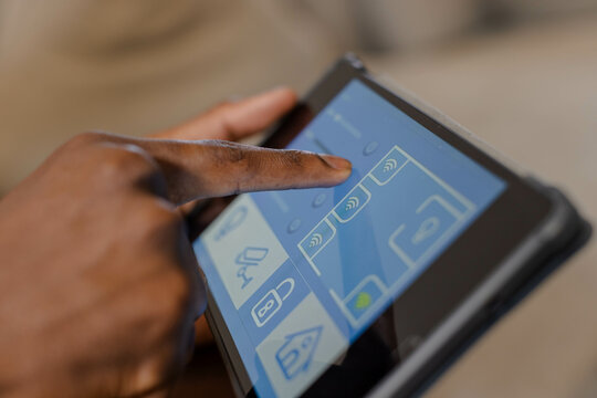 African American man's hand tapping touchscreen tablet in living room, with smart home UI icons