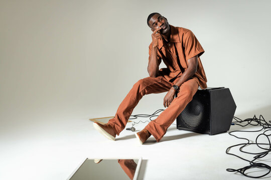 Sitting African American man leaning cheek on hand at white studio, with mirror panel, copy space