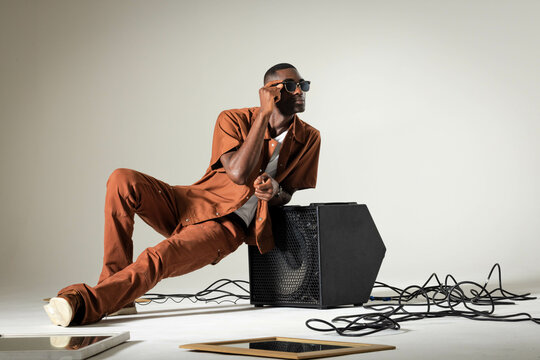 Leaning African American man adjusting sunglasses in studio, with amplifier, cables and tablets