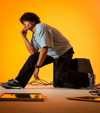 Posing African American man kneeling on speaker cabinet in studio, with cables and mirror panels