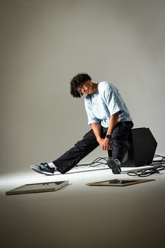 Leaning African American man stretching legs on speaker in studio, with artwork and audio cables