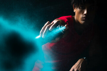 African American man spraying blue aerosol mist in dark studio, glowing aura and copy space