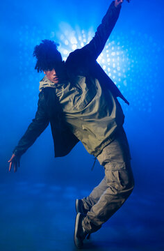 Dancing male dancer in twenties wearing leather jacket in fog-filled studio, with blue LED lights