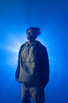 Standing man facing upward with eyes closed in photography studio, highlighting blue light beams