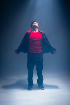 Posing African American man wearing red top and black jacket with chain in studio under spotlight
