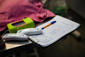 On a metal table are veterinary instruments and a medical chart with handwritten notes indicating current treatments and procedures at the veterinary clinic. The patient's chart lies on the table.