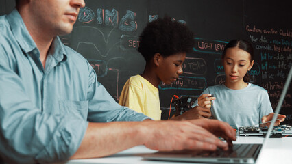 Young student fixing controller while teacher programing engineering code at STEM class. Closeup of...