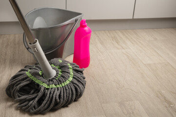 A mop for mopping floors next to a bucket of water and detergent. Home and office cleaning concept with copy space
