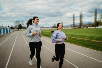Two female friends running or jogging on stadium doing sport activities