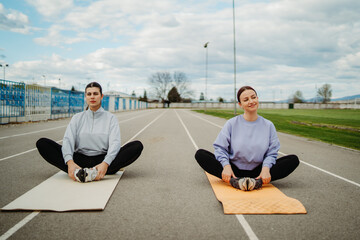 Two female friends stretching on stadium doing sport activities