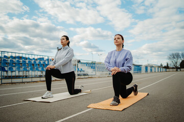 Two female friends stretching on stadium doing sport activities